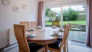 Ein Esszimmer mit einem runden Tisch, sechs Holzsesseln und Blick auf einen Garten durch eine Glastür.