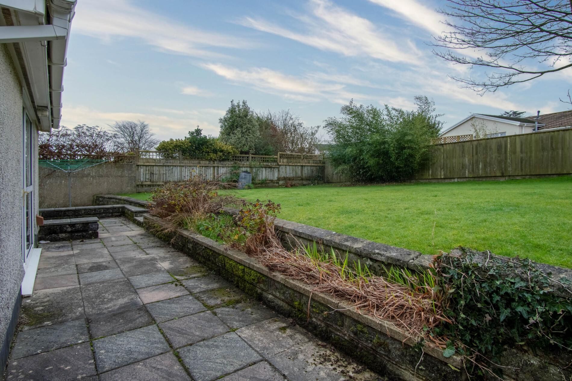 A backyard with a stone pathway leading to a grassy lawn, surrounded by a wooden fence and various plants.