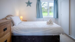 Ein Schlafzimmer mit einem Bett, einer Holzkommode, einem Nachttisch mit Lampe, einer Sterne-Dekoration und einem Fenster mit Vorhängen.