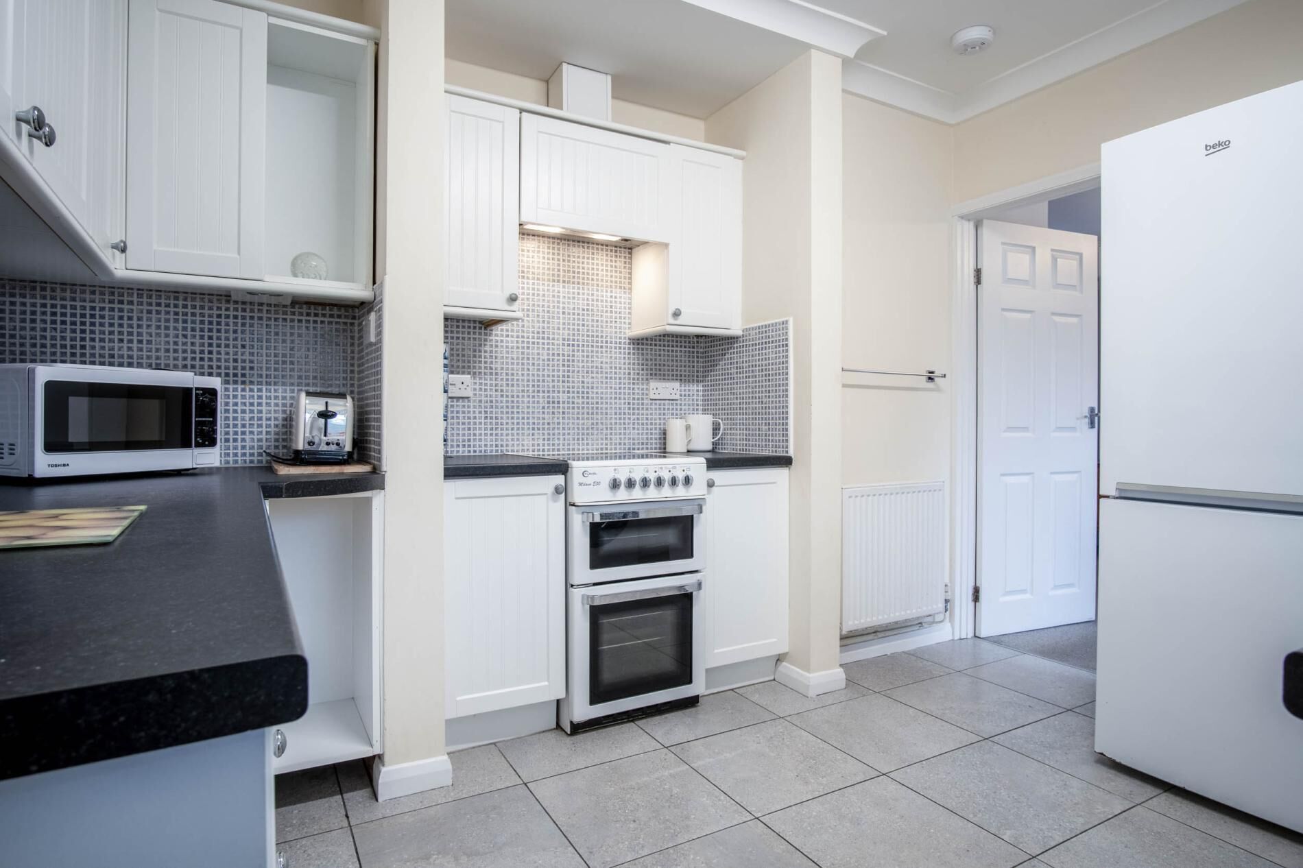 A kitchen with white cabinets, a microwave, a toaster, an oven, and a refrigerator.