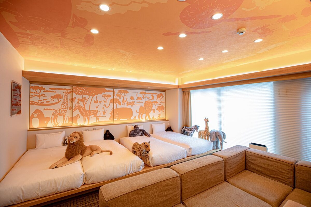 A hotel room with a large bed, a sofa, and a mural of animals on the wall.