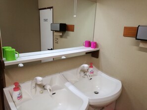 A bathroom with two sinks, a mirror, and a shelf with green and pink mugs. - Business Inn Mizuho Ryokan (Koriyama)