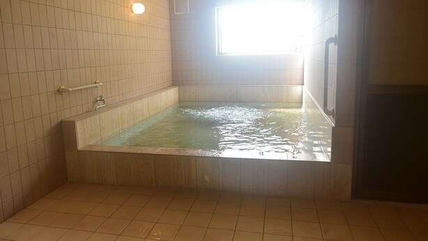 Een badkamer met een groot bad, betegelde wanden en een raam dat natuurlijk licht binnenlaat.