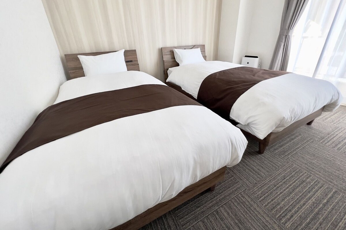 A hotel room with two beds, a large window with curtains, and a carpeted floor.