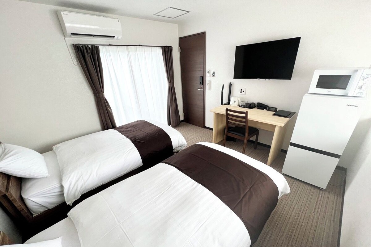 Habitación de hotel con dos camas, un escritorio, televisor y minibar.