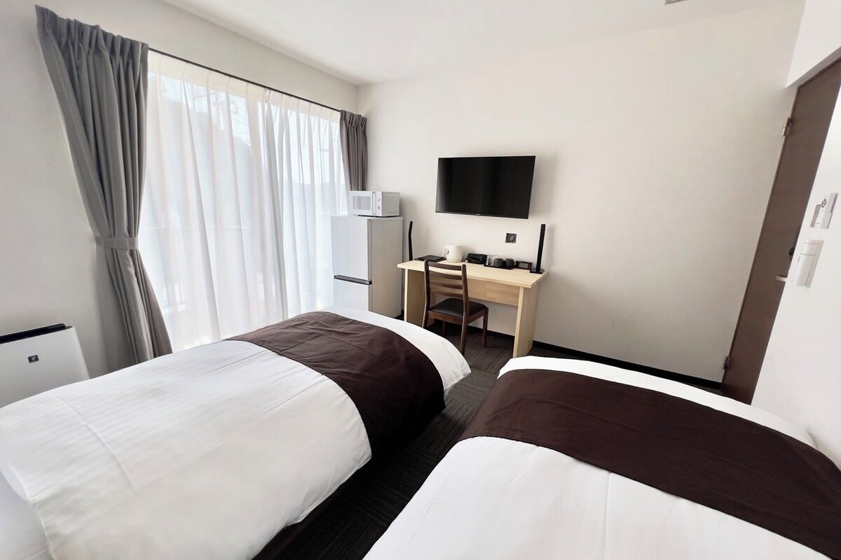 A hotel room with two beds, a desk, a TV, and a minibar.
