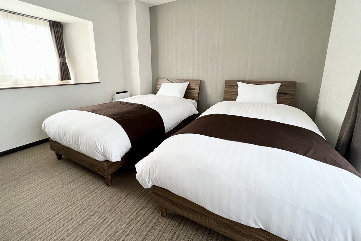 Una habitación de hotel con dos camas, una ventana con cortinas y piso alfombrado.