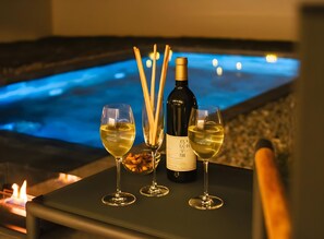 A table with two glasses of white wine, a bottle of wine, and a bowl of nuts. In the background, there is a pool with a blue hue and a fire. - Kenken Reto Private Villa (Motobu)