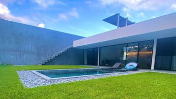 A modern house with a swimming pool, a grassy lawn, and a staircase leading to a second floor.