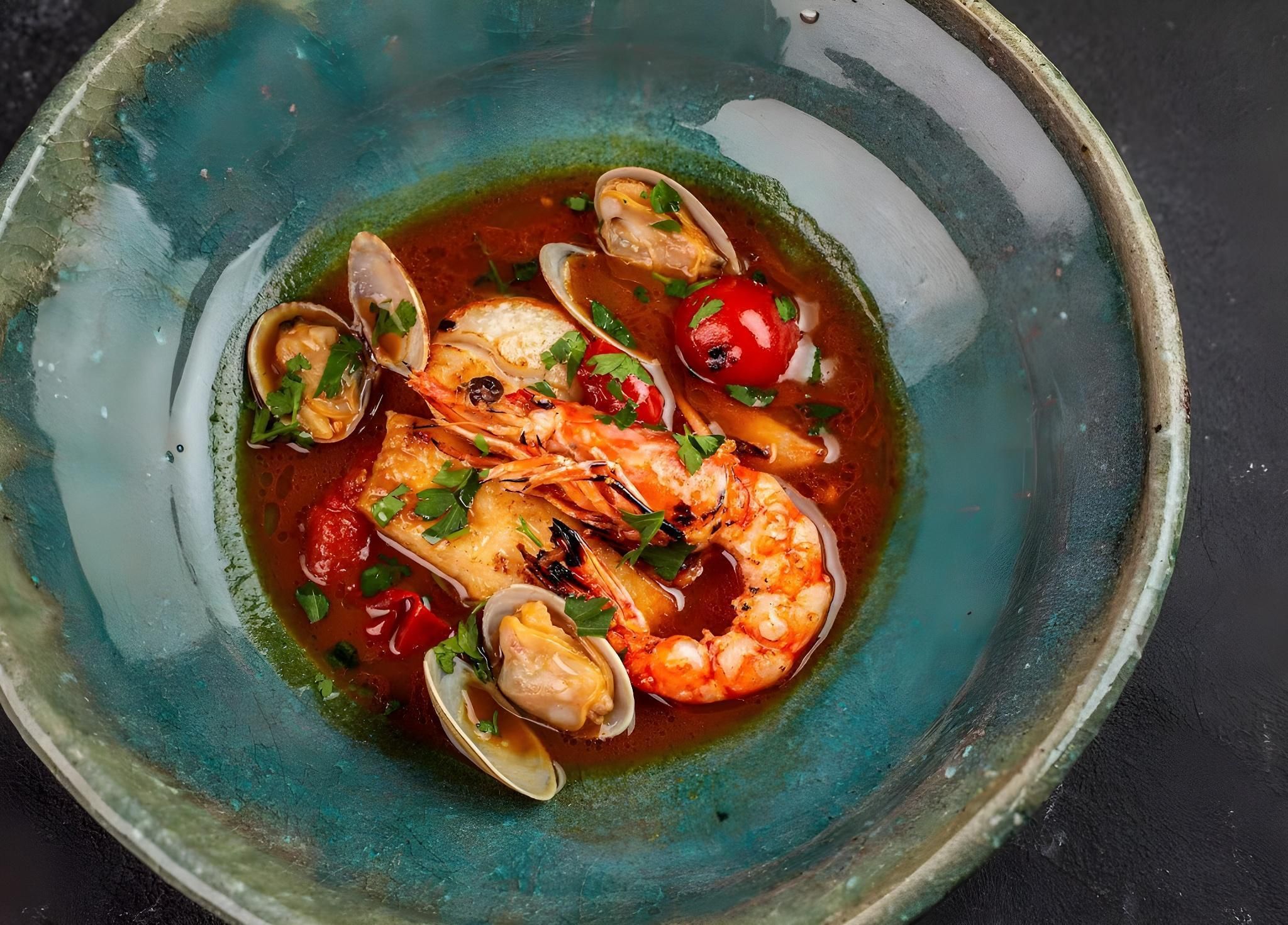 A seafood dish with clams, shrimp, and cherry tomatoes in a ceramic bowl.