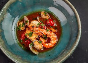 A seafood dish with clams, shrimp, and cherry tomatoes in a ceramic bowl. - Kenken Reto Private Villa (Motobu)
