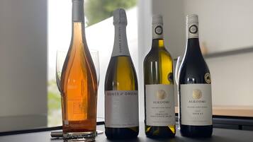 Four wine bottles and a wine glass on a table by a window.