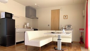 Een moderne keuken met een magnetron, fornuis en koelkast. Er is een witte werkbank en een tafel met een fles handdesinfectiemiddel.