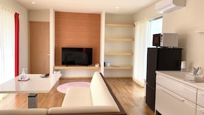 Een moderne woonkamer met een flatscreen televisie, een wand van houten panelen, een witte bank, een keuken met een koelkast en een eettafel met een roze vloerkleed.