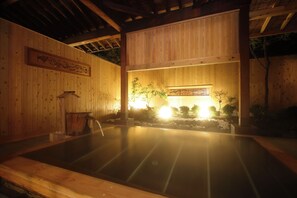 Un bain traditionnel en bois, doté d’une source d’eau chaude, de poutres en bois et d’une œuvre d’art encadrée au mur.