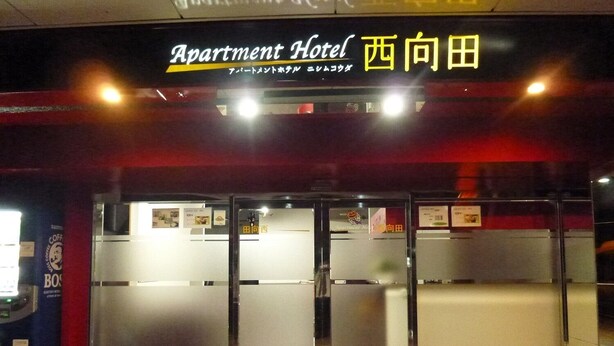 The entrance to an apartment hotel with a sign indicating it's open. - Apartment Hotel Nishimukoda (Satsumasendai)
