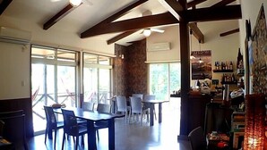 A spacious dining area with a high ceiling and exposed beams, a bar area with shelves of bottles, and large windows allowing natural light. - Uminchu Style Amami (Setouchi)
