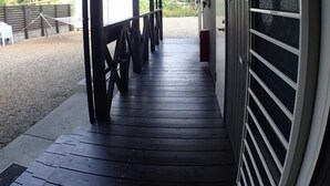 A covered outdoor area with a wooden deck, metal railings, and a view of a hilly landscape. - Uminchu Style Amami (Setouchi)