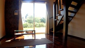 A spacious room with a wooden floor, a bench, and a staircase leading to an upper level. - Uminchu Style Amami (Setouchi)