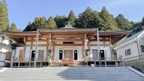 Un edificio japonés tradicional con entrada de madera, una escalera de piedra y vistas a árboles circundantes.