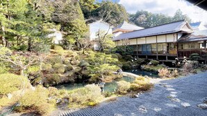 Un edificio japonés tradicional con un estanque de carpas y abundante vegetación.