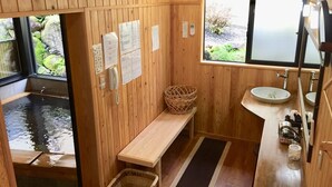 A wooden interior with a wooden bench, a sink, and a window with a view of greenery. - Yunomori Kusu (Kusu)
