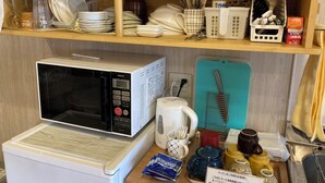A kitchen area with a microwave, coffee maker, and various kitchen utensils on shelves. - Yunomori Kusu (Kusu)