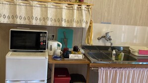 A compact kitchen with a microwave, kettle, sink, and a small trash bin. - Yunomori Kusu (Kusu)