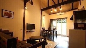 A cozy living room with a sofa, a TV mounted on the wall, and a dining area with chairs and a table. - Yunomori Kusu (Kusu)