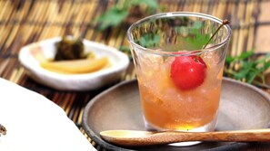 Un vaso de bebida helada con cereza en el borde, una cuchara y un pequeño plato con un objeto amarillo al fondo.