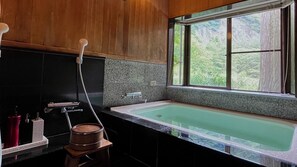 Un baño moderno con una bañera grande, un box de ducha de madera y un ventanal con vistas a la vegetación.