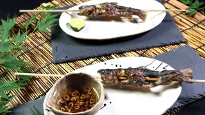 Un plato con brochetas de pescado a la parrilla y un tazón de bocadillos fritos, acompañado de una cuña de lima.