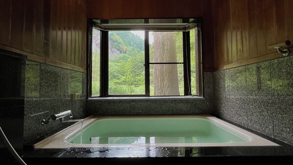 Un baño con bañera, ventana y vista a la vegetación.