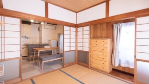 A traditional Japanese room with tatami flooring, a low wooden table, a sofa, and a wooden cabinet. - Tomie Yado (Goto)