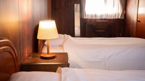 Ein Hotelzimmer mit zwei Betten, einem Holznachttisch mit Lampe sowie einem Schreibtisch und einem Stuhl.