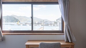 Ett rum med ett skrivbord i trä och ett fönster med utsikt över en hamn med båtar och kullar.