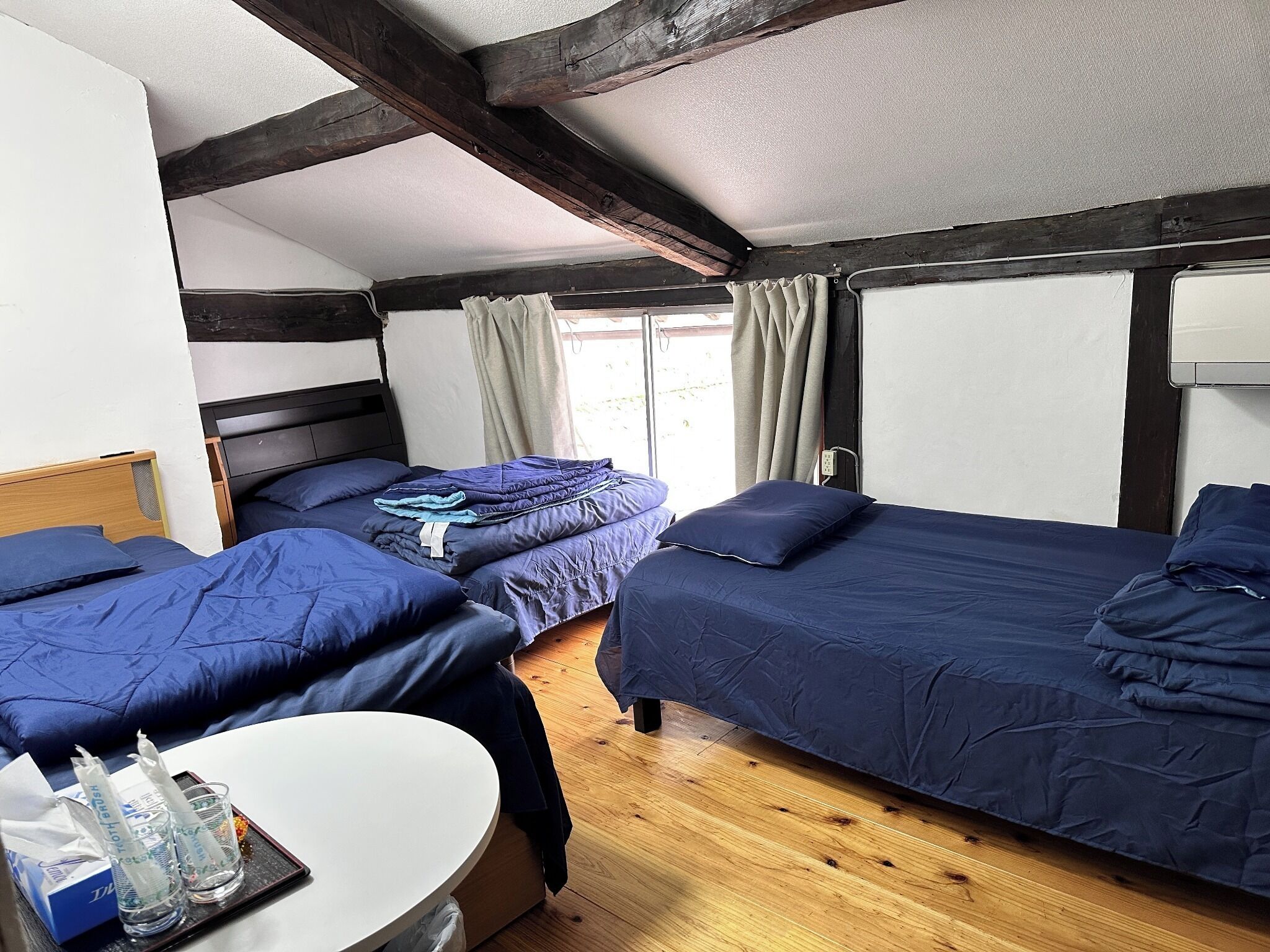 Una habitación con dos camas, una mesita y una ventana con cortinas.