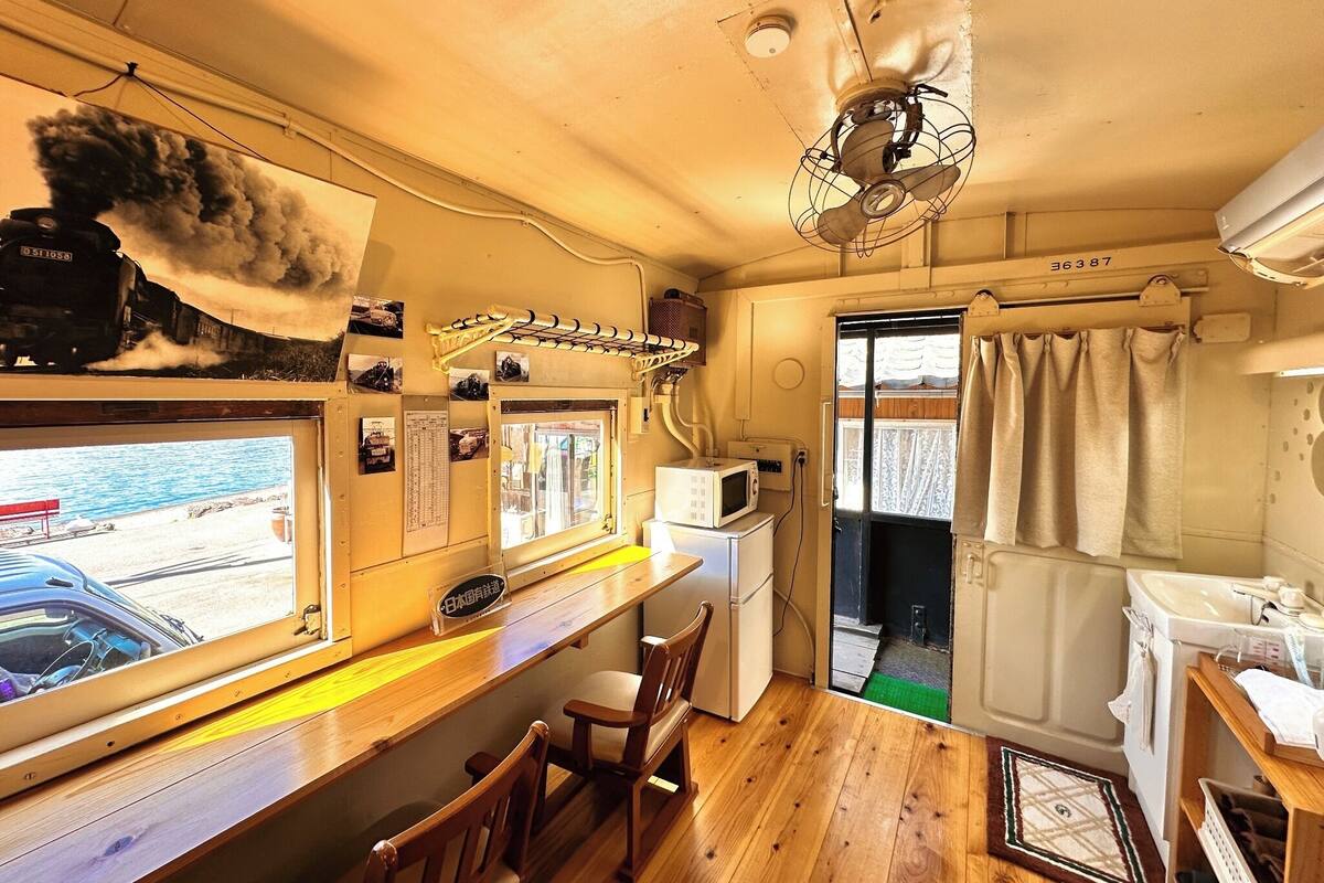 A compact kitchen with a wooden countertop, a microwave, a fan, and a view of the sea.
