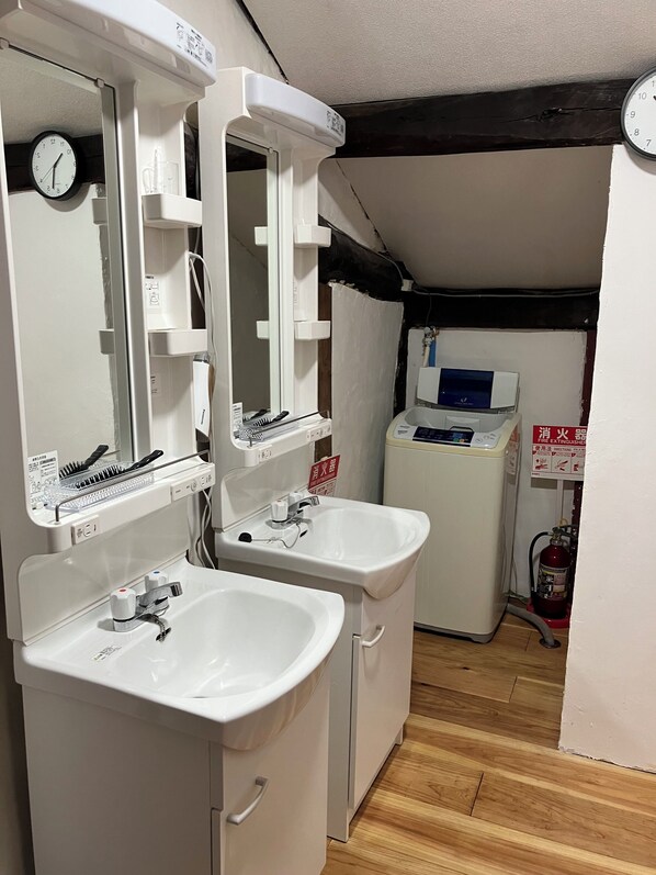 A bathroom with two sinks, a mirror, a clock, and a fire extinguisher.