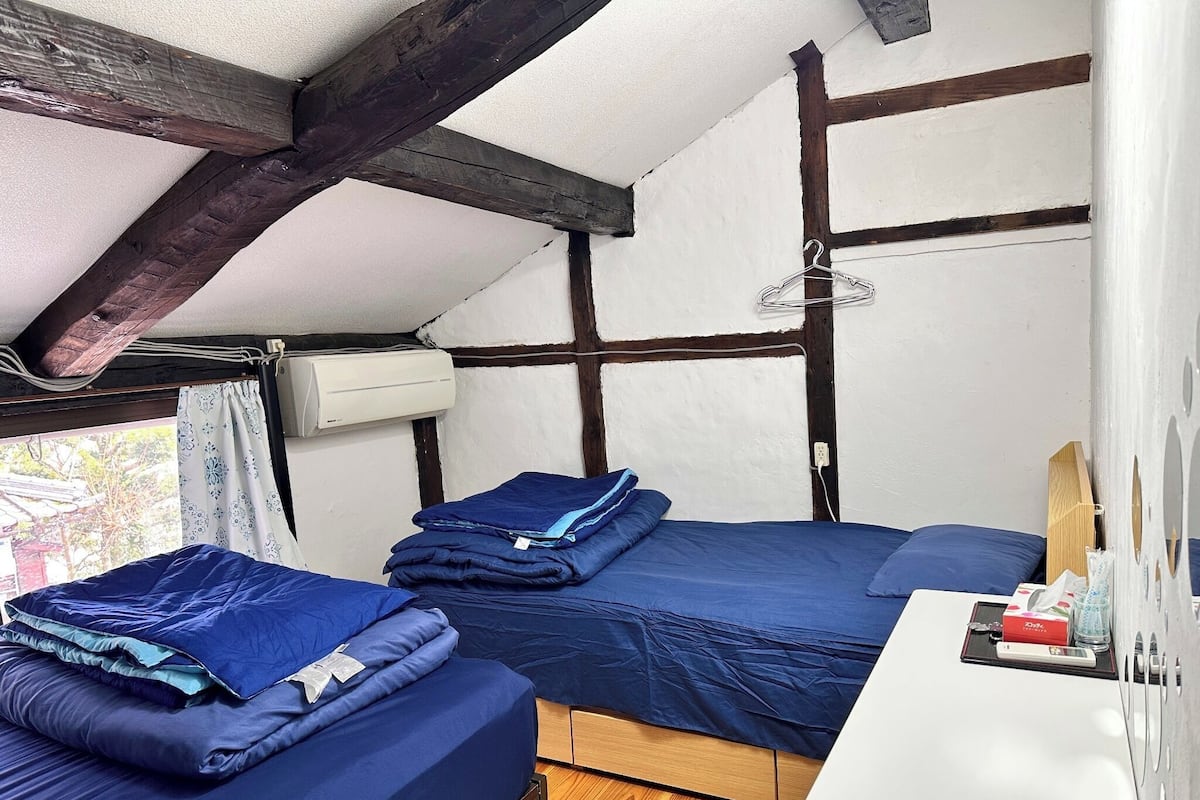 A small, cozy room with two beds, a desk, and a window.