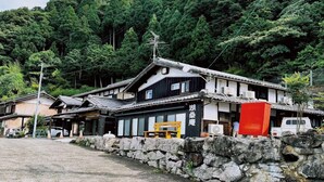 Edificio japonés tradicional con un muro de piedra en primer plano, un banco de madera y un objeto rojo a la derecha.