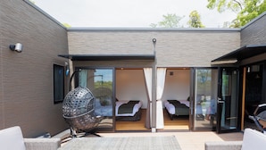 Un bâtiment moderne à la façade en briques, doté de grandes portes-fenêtres coulissantes qui donnent sur une chambre avec deux lits, et d'un fauteuil en osier à l'extérieur.