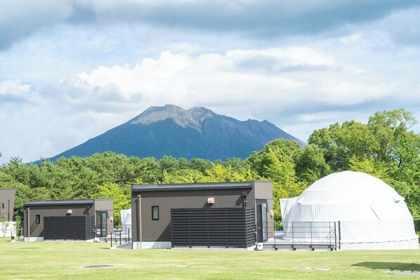 Ein modernes Gebäude mit Garage und Kuppel, vor einer Berglandschaft mit üppigen Bäumen.