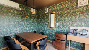 Un coin repas avec une table et des chaises en bois, un petit espace cuisine équipé d’un évier et d’une bouilloire, et une fenêtre donnant sur un beau paysage.