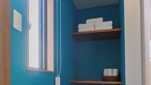 Une petite buanderie aux murs bleus, avec un plancher en bois, une fenêtre, une étagère avec des serviettes, un panier et un étendoir en métal.