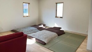 Une petite pièce lumineuse, avec un lit, deux fenêtres et une chaise rouge.