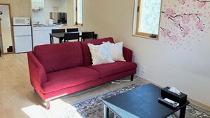 Un espace de vie compact avec un canapé rouge, une petite table et un coin cuisine à l’arrière-plan.