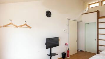 Ett hotellrum med en säng, en tv, trägalgar, en klocka, en brandsläckare och en dörr.