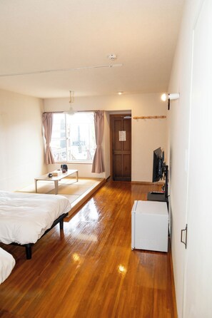 A hotel room with a bed, a small table, a TV, and a window with curtains. - Beach Front Auberge Litore (Shimoda)