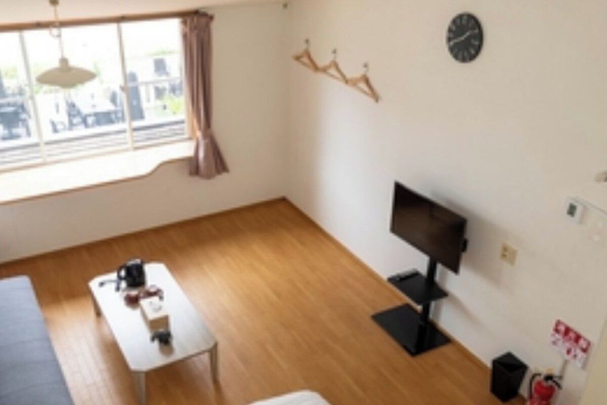 A room with two beds, a TV, a small table, and a window with curtains.